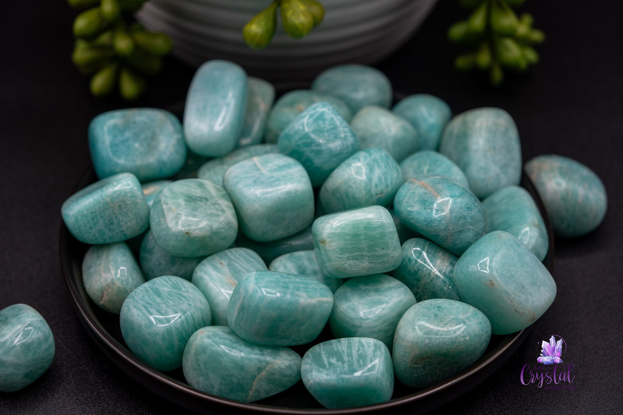 Polished amazonite tumbled stones on a black plate with plants, crystal decor