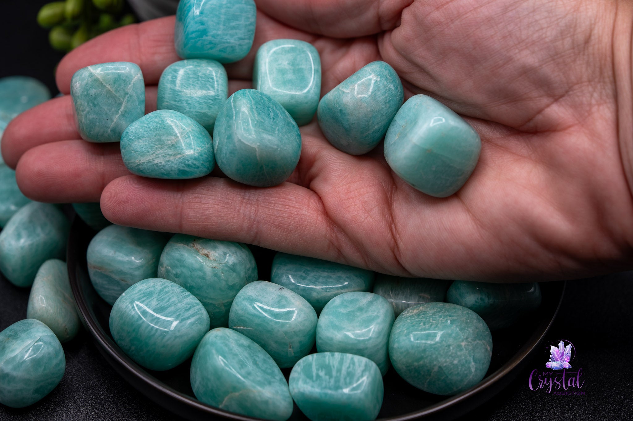 Hand holding polished amazonite stones in a bowl, crystal healing gemstones display