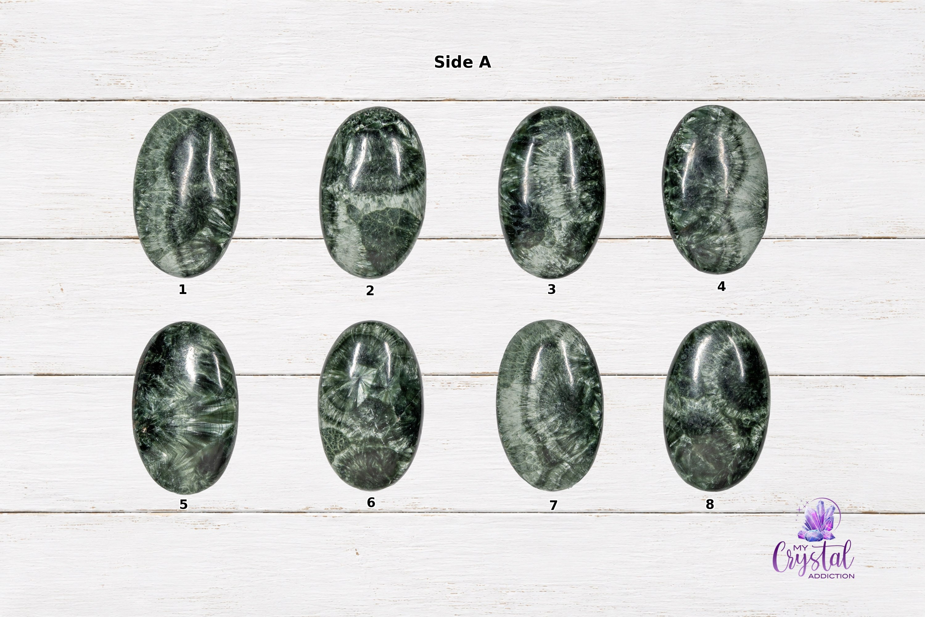 Side A view of numbered polished Seraphinite mini palm stones on a white wood background.