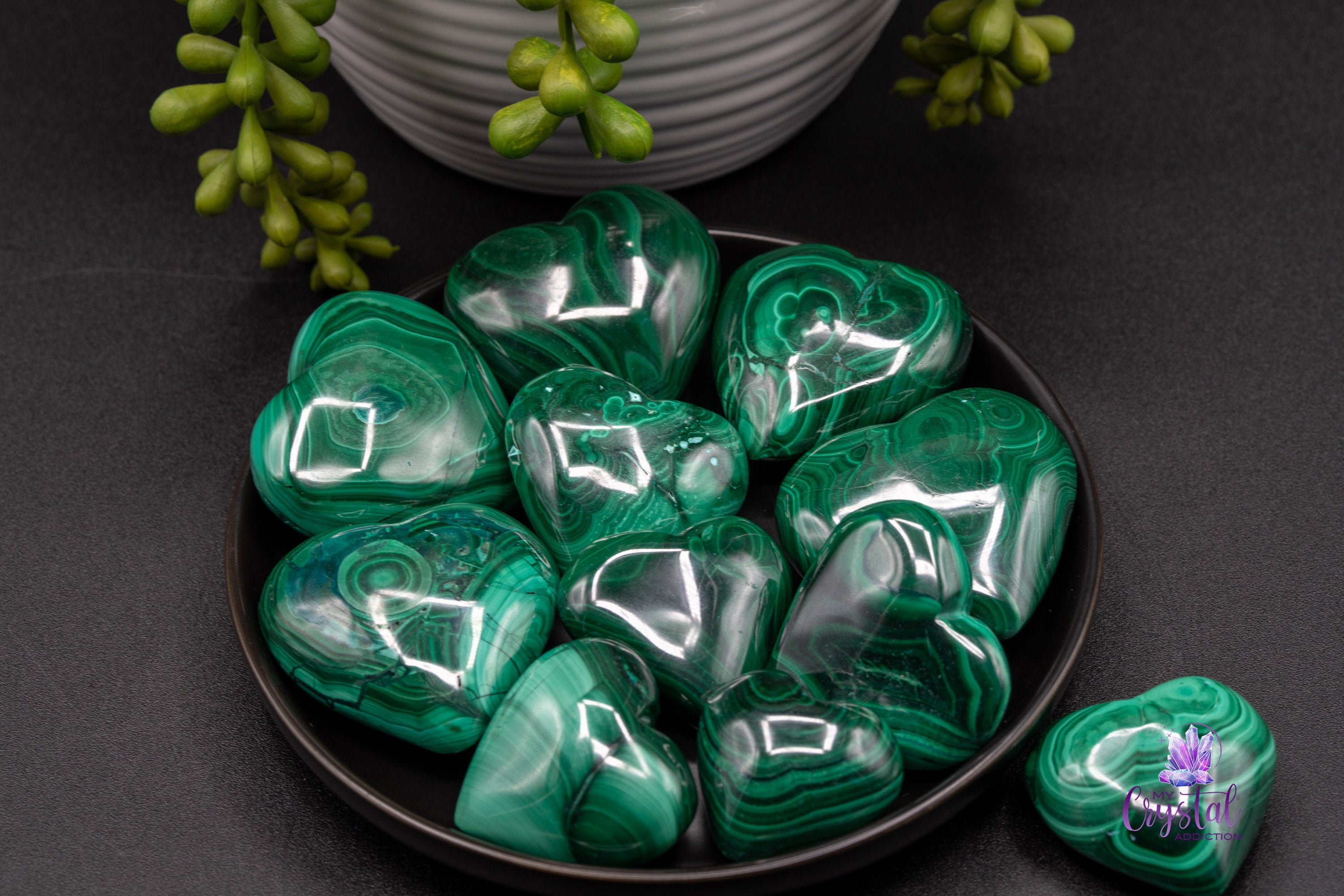 Polished green malachite heart carvings with banded patterns arranged in a black dish.